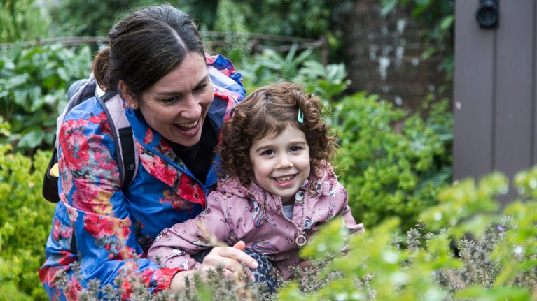 A mother and her daughter smile and point at plants in a kitchen garden